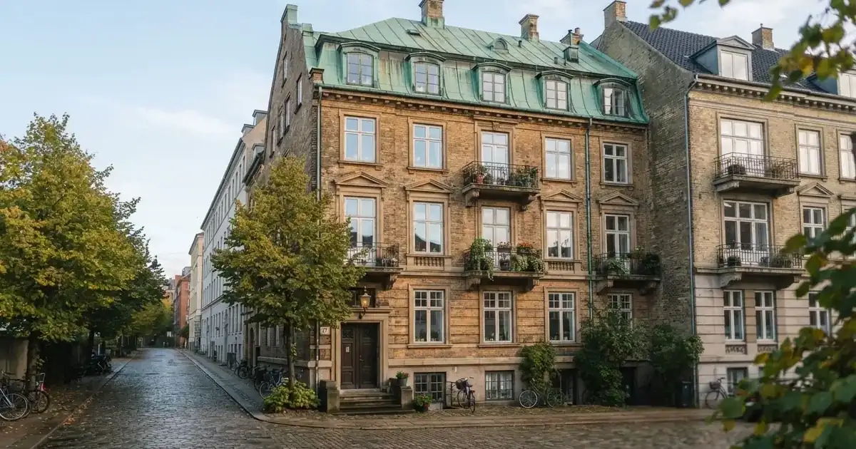 En historisk bygning i København med grønt kobbertag og høje vinduer i klart dagslys, set fra gaden uden mennesker.