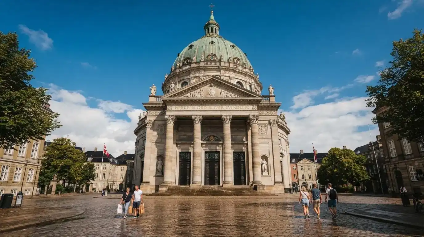 En historisk bygning i København med grøn kobbertag og kolonner i klart dagslys, set fra pladsen foran.